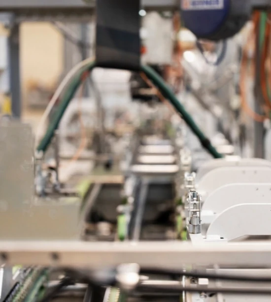 Nahaufnahme einer Produktionslinie mit Förderbändern und Maschinen in einem industriellen Umfeld; Fokus auf automatisierte Technik.